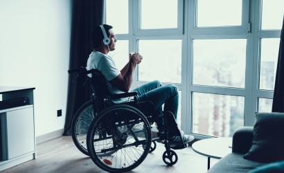 Niepełnosprawny mężczyzna słucha muzyki i pije kawę na nowoczesnym wózku inwalidzkim nosi słuchawki i patrzy na duże panoramiczne okno w salonie lub szpitalu